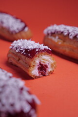 beautiful delicious eclair with coconut cream filling and raspberry jelly.  confectionery, sweets. close up. coconut flakes. modern popular dessert. european pastry