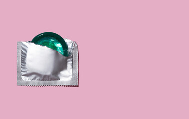 Condom half out of package on a pink background. A condom use to reduce the probability of pregnancy or sexually transmitted disease (STD). Safe sex and reproductive health concept. Top view. 