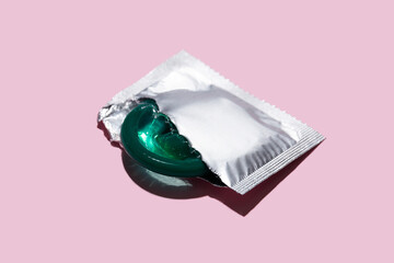 Condom half out of package on a pink background. A condom use to reduce the probability of...