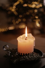 Christmas and New Year cozy  atmosphere. white candle in a black candlestick is burning against the background of blurry Christmas tree garlands. candle flame
