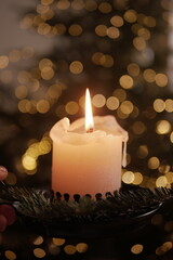 Christmas and New Year cozy  atmosphere. white candle in a black candlestick is burning against the background of blurry Christmas tree garlands. candle flame

