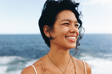 Close-up of smiling woman with wavy hair and bohemian jewelry at the seaside
