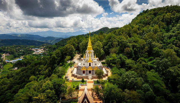 Aerial view of Phrathat Chedi Srinagarindra Stit Maha Santi Khiri Temple and Pagoda surrounded by forested mountains under a cloudy sky, Mae Salong Nok, Chiang Rai District, Thailand.