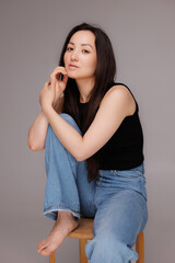 Brunette asian woman posing while sitting on chair on grey background