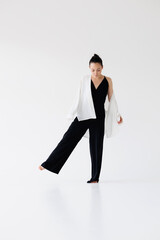 Stylish asian model in black jumpsuit and shirt standing on grey background