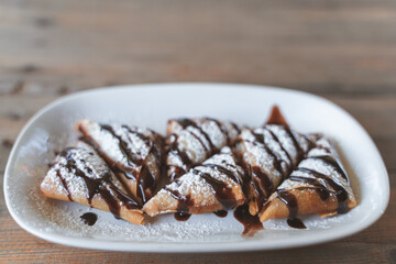 A plate of delicious pastries drizzled with chocolate sauce and dusted with powdered sugar, served on a rustic wooden table.