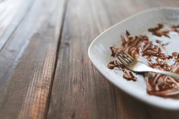 A close-up of a white plate with chocolate remnants and a fork on a rustic wooden table, creating a cozy and relaxed atmosphere.
