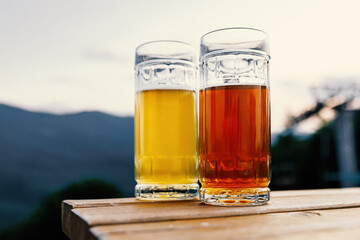 Two glasses of beer, one pale and one amber, bask in the warm glow of a sunset.
