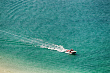View of motorboat cruising on turquoise ocean with sandy beach and gentle waves, dubai, united arab emirates.