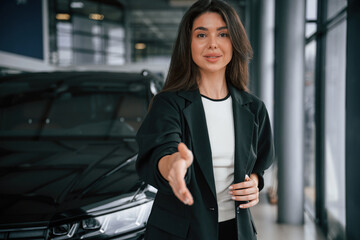 Giving a hand to shake, making a deal. Saleswoman in car showroom, selling automobile