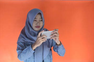 Portrait of a young Asian Muslim woman playing games at home on an orange background