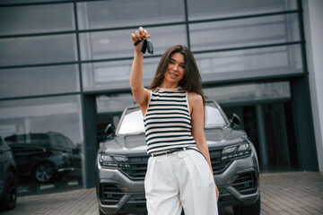 Keys for the new car. Happy owner. Attractive young woman is outdoors near her brand new car