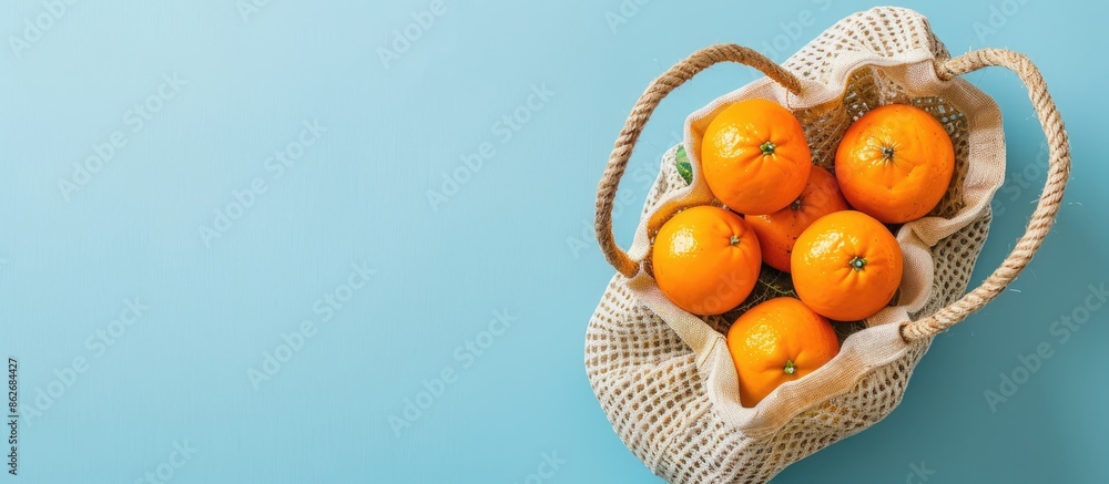 Poster top view flat lay composition featuring a beige string bag filled with oranges on a blue background,
