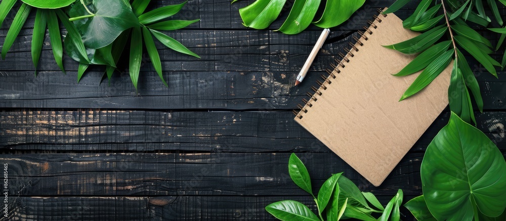 Aufkleber top view of a notebook on a black wooden surface with green leaves, creating a stylish office deskto