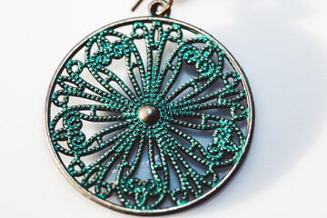 Circular green and gold pendant with intricate design. Earring is made of metal and has a shiny, metallic look