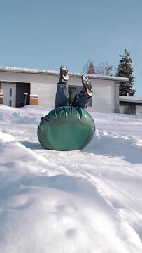 Funny clumsy guy trying to ride a snowtube from the mountain but falls on his back. Adult childhood concept Vertical shot.