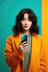 Fototapeta premium A woman in a yellow coat holding a cell phone. The photo is in a blue and orange color scheme