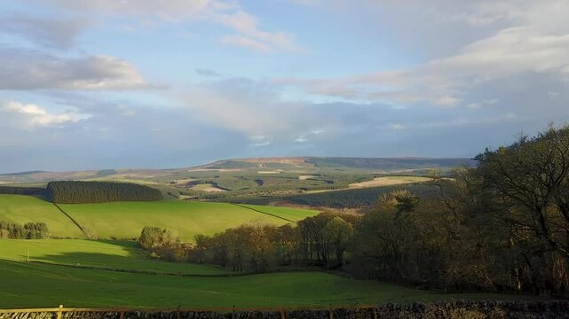 Aerial view of rolling hills and lush fields under vibrant sky at Chesters Brae, Hawick, Scotland, United Kingdom.