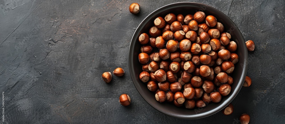 Poster overhead shot of a bowl brimming with hazelnuts against a copy space image.