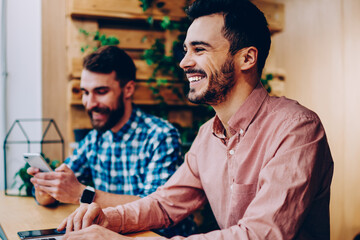 Cheerful male student laughing at funny joke learning on laptop computer spending time in campus with friend,happy prosperous freelancers satisfied with productive job using modern technologies