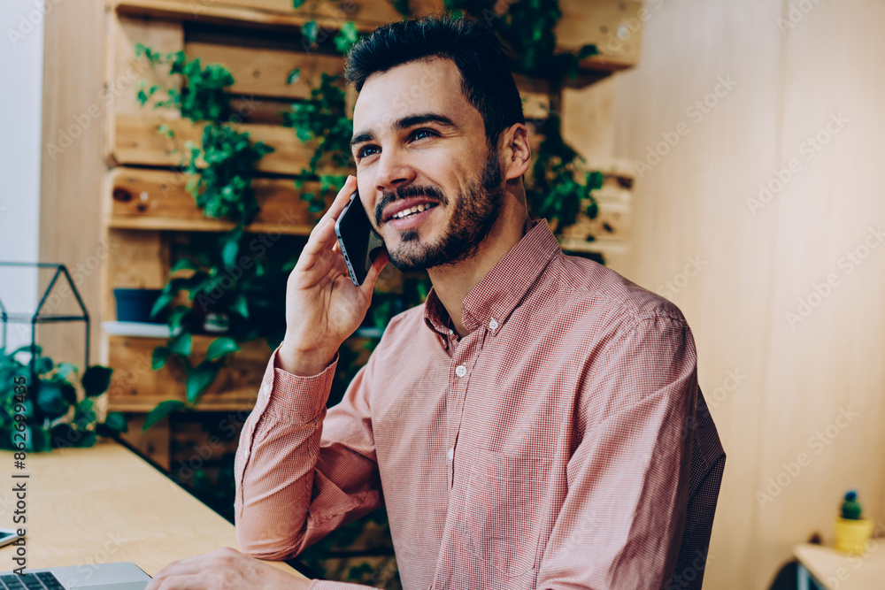 Poster smiling handsome man having telephone conversation during remote job via laptop computer, cheerful h