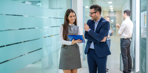 Beautiful elegant business people discussing over documents while standing in glass office hallway.
