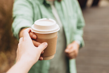 Woman gives paper coffee cup. Take away or delivery concept. Copy space. Place for your text or logo on mug, mockup. Woman takes a cup
