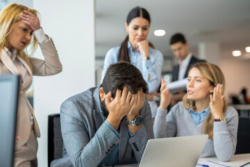 Businessman is covering his face with his hands while his concerned female colleagues lecturing him...