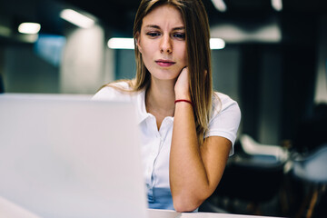 Pensive female student watching tutorial concentrated on analyzing information for e-learning on...