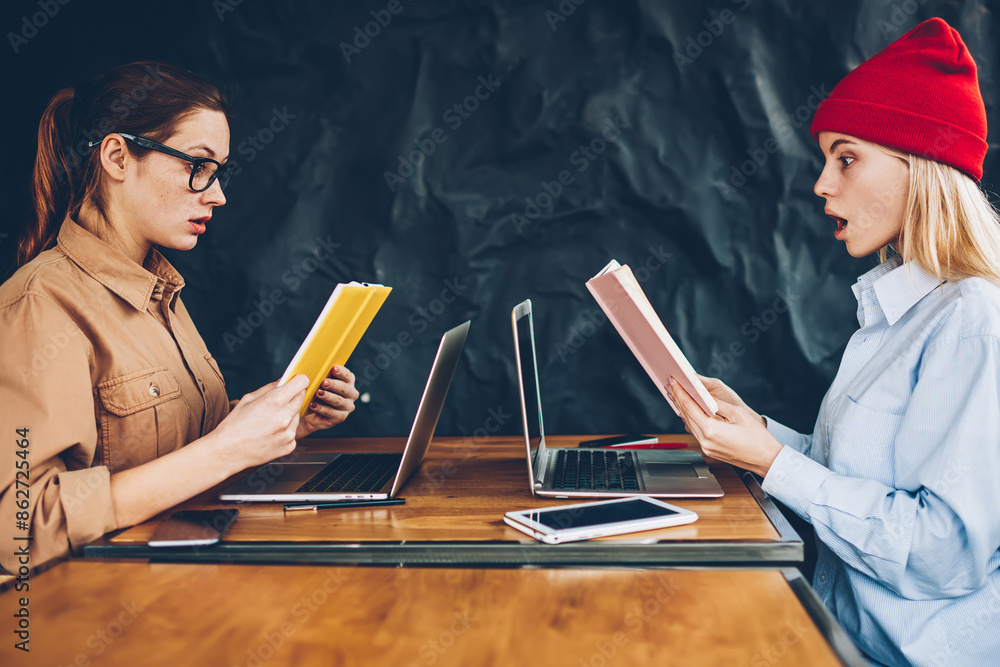 Poster side view of excited two students shocked with confused information in textbook studying together at