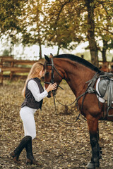 Fototapeta premium A young female equestrian stands near her horse and prepares for a competition.