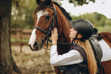 A young female equestrian stands near her horse and prepares for a competition.
