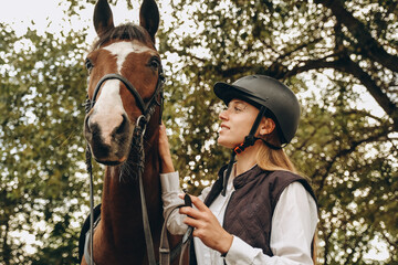 A young female equestrian stands near her horse and prepares for a competition.