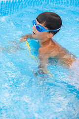 Boy in glasses swimming with the board in the outdoor pool. Summertime. 