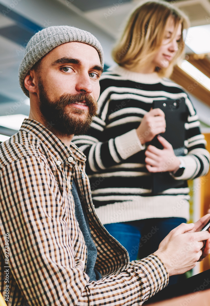 Poster half length portrait of handsome bearded employee in cool hat downloading application from network o