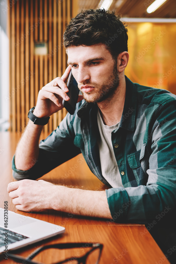 Aufkleber young handsome male designer having mobile conversation via application on smartphone while watching