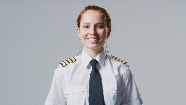 Smiling young female airline pilot or ship captain wearing uniform in front of plain studio background - shot in slow motion