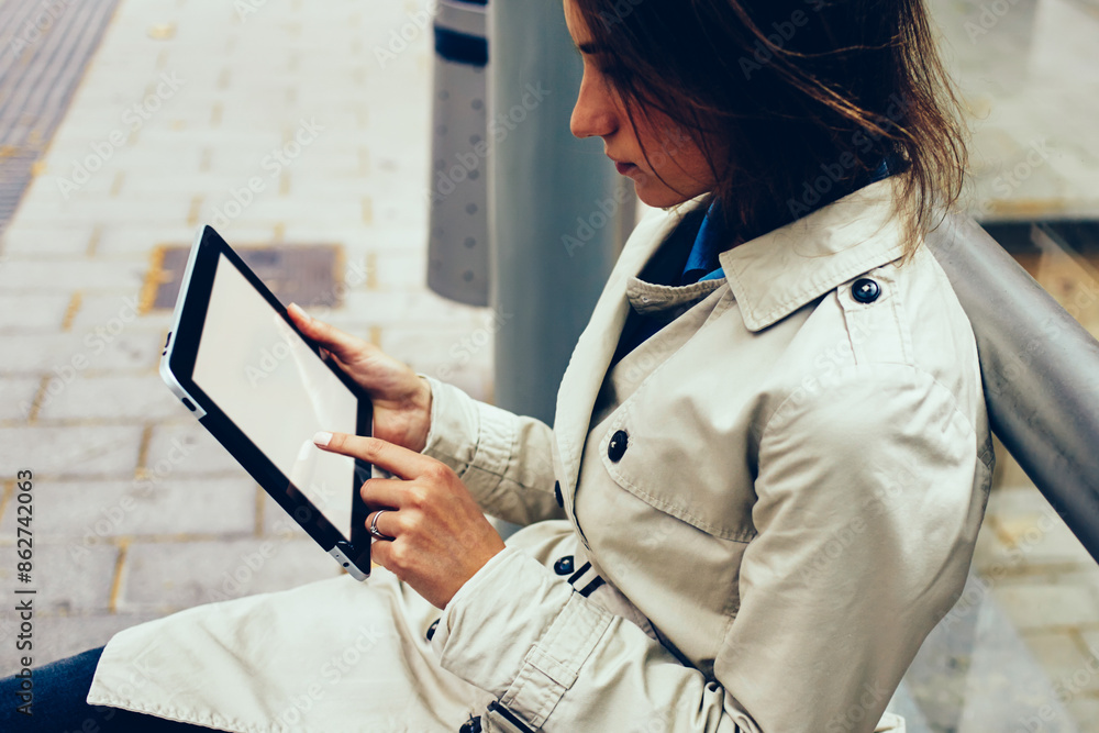 Poster side view of pensive female hipster blogger touching with finger mock up screen of modern touch pad 