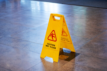A caution sign warning of wet floor in yellow displayed on tiled surface