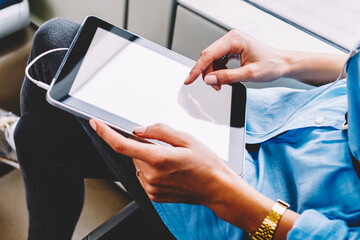 Cropped view of young woman choosing audio song in playlist downloaded on modern touch pad with earphones.Female person touching with finger on blank screen area of digital tablet using transport wifi