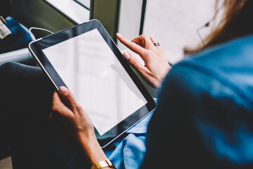 Cropped back view of female person holding modern touch pad device with copy space display for your website content.Young woman with tablet in hands using public transport wireless internet in tram