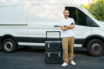 Young handsome handyman with tools box near trunk outdoors