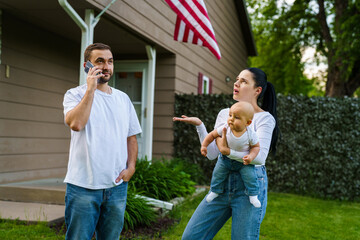 Naklejka premium Young pretty family standing in front of house outdoors. Father talk phone and bother mother