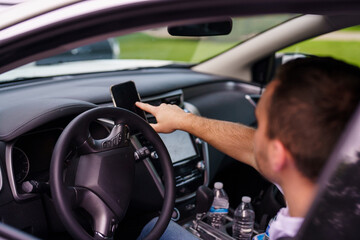 Naklejka premium Young man riding the car in the city while using mobile phone and typing message.