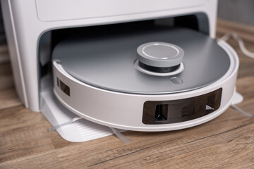 A white robot vacuum cleaner with a silver base. The robot is on a wooden floor