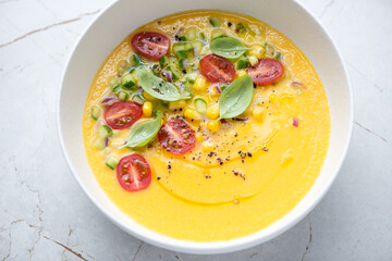 Chilled gazpacho made of sweet corn, yellow tomatoes and bell peppers, horizontal shot on a white granite surface, middle close-up