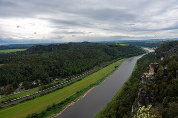 A river with a train passing by. The train is carrying a lot of cars. The sky is cloudy