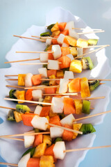 Buffet with varied fruits skewers in a tray. Detail of a ceramic tray with cubes of assorted pieces of fruits.