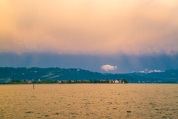 Germany, Lindau island village houses, bodensee lake water panorama, view to mountains, alps, nature landscape after sunset on stormy day with magical glowing sky