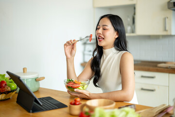 A woman is eating a salad in front of a laptop